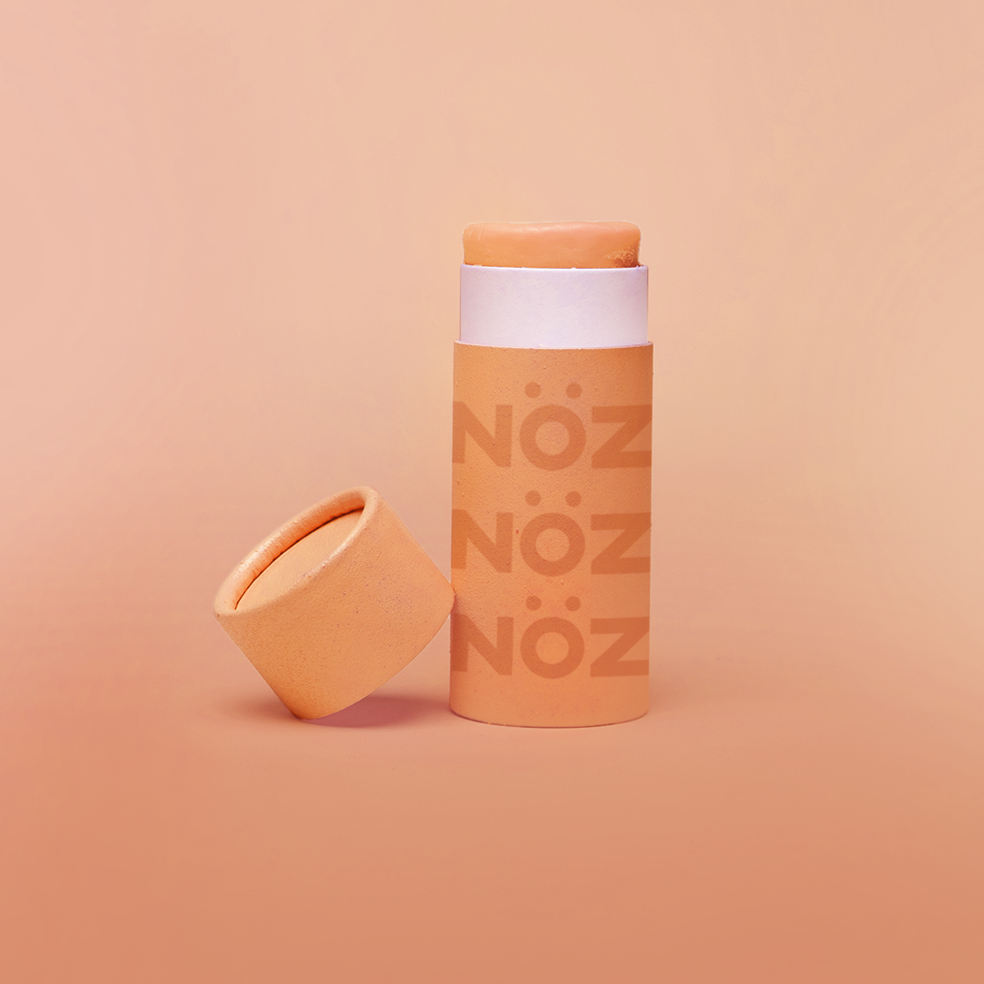 front view of orange Noz product with the cap off and leaning on the product, fun colorful sunblock stick is showing