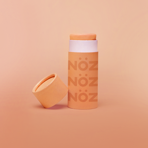 front view of orange Noz product with the cap off and leaning on the product, fun colorful sunblock stick is showing