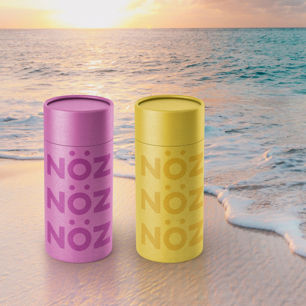 Two Noz sunscreens in purple and yellow on the beach during sunset near the water